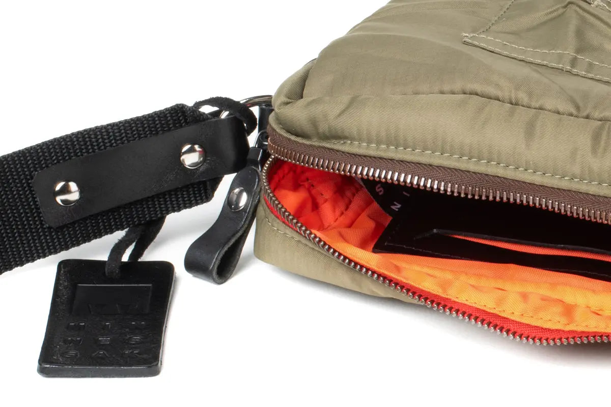 Olive bag with a black strap and orange interior on a white background