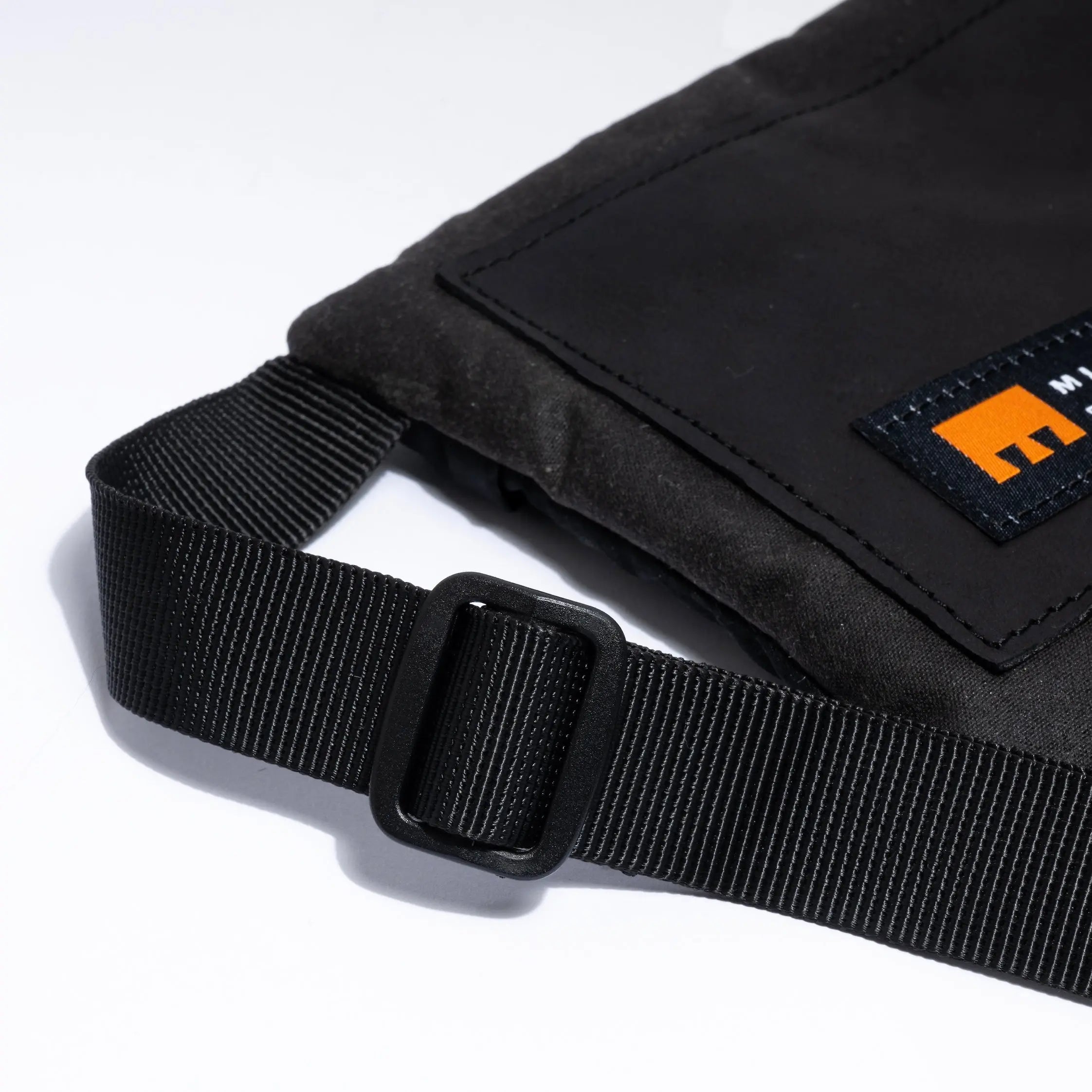 Small cross body bag in black showing strap detail and Minnessak logo on white background