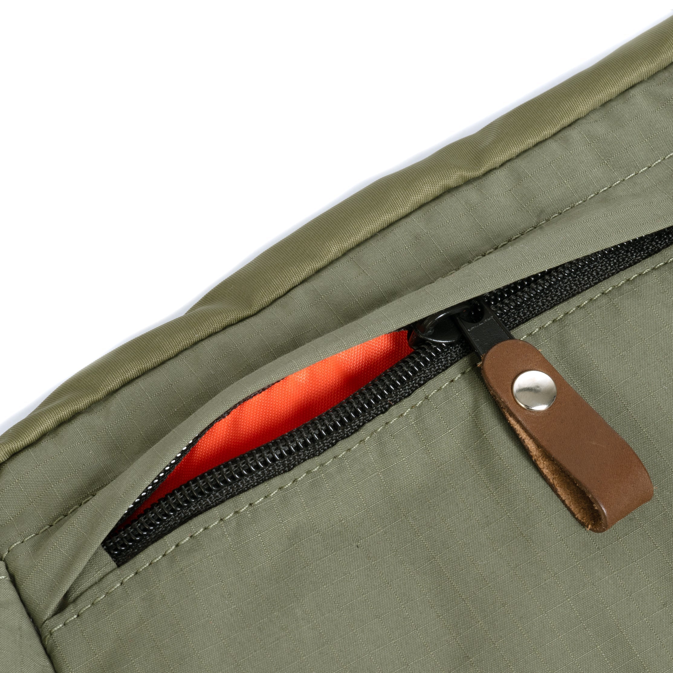 Close-up of a olive jacket with a zipper pocket featuring a brown pull tab.