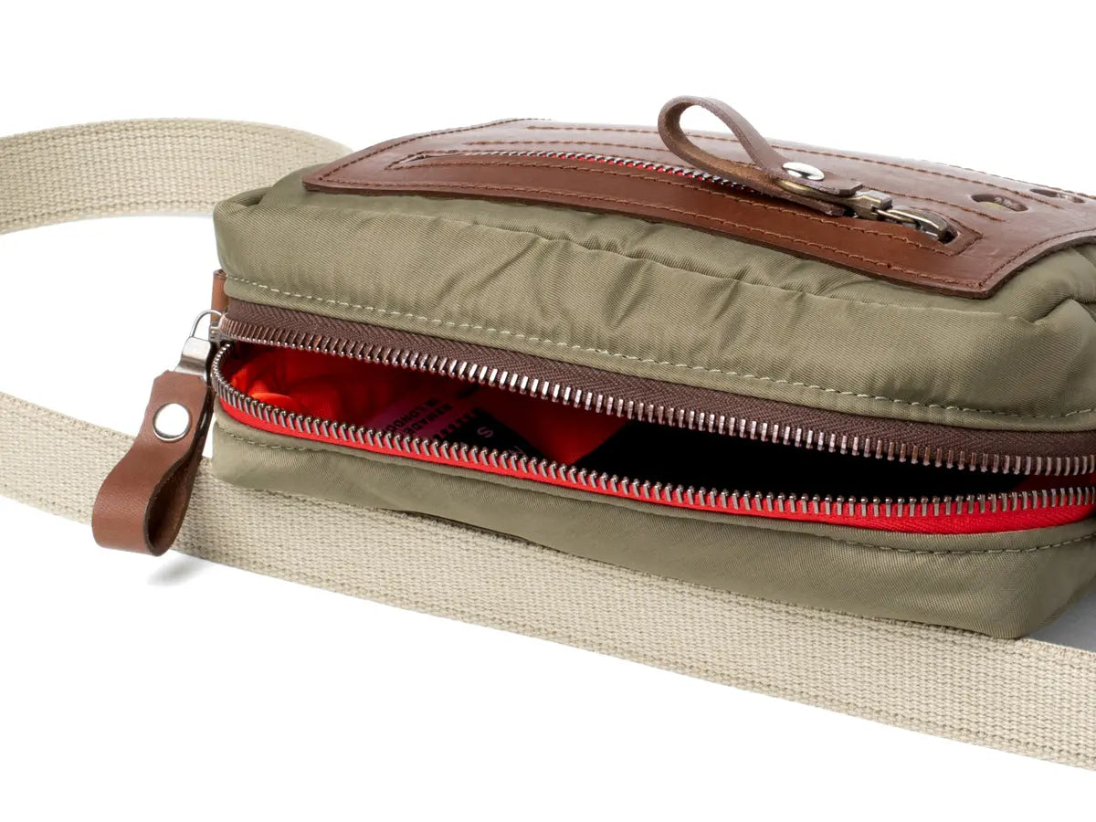 Olive bag with a brown zipper and beige strap on a white background
