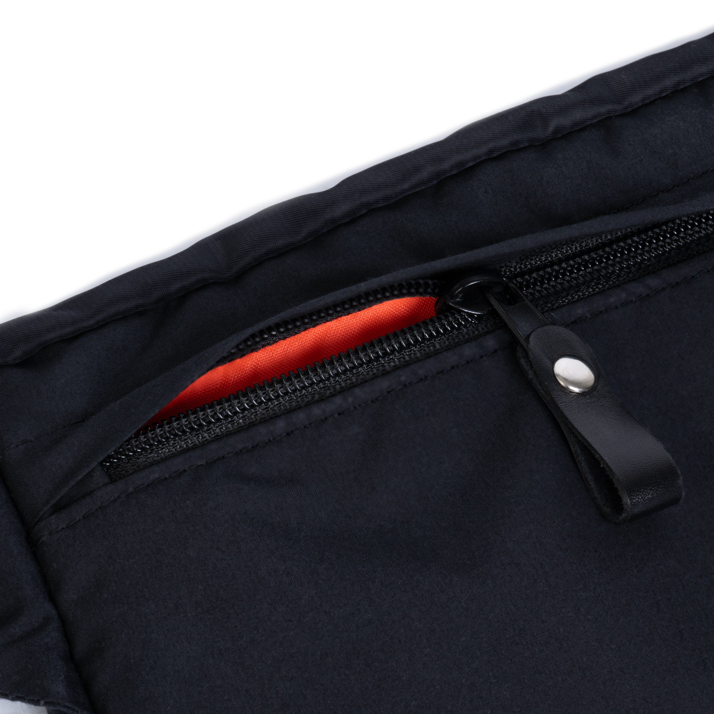 Close-up of a black bag with a zipper partially open, revealing an orange interior on a white background.