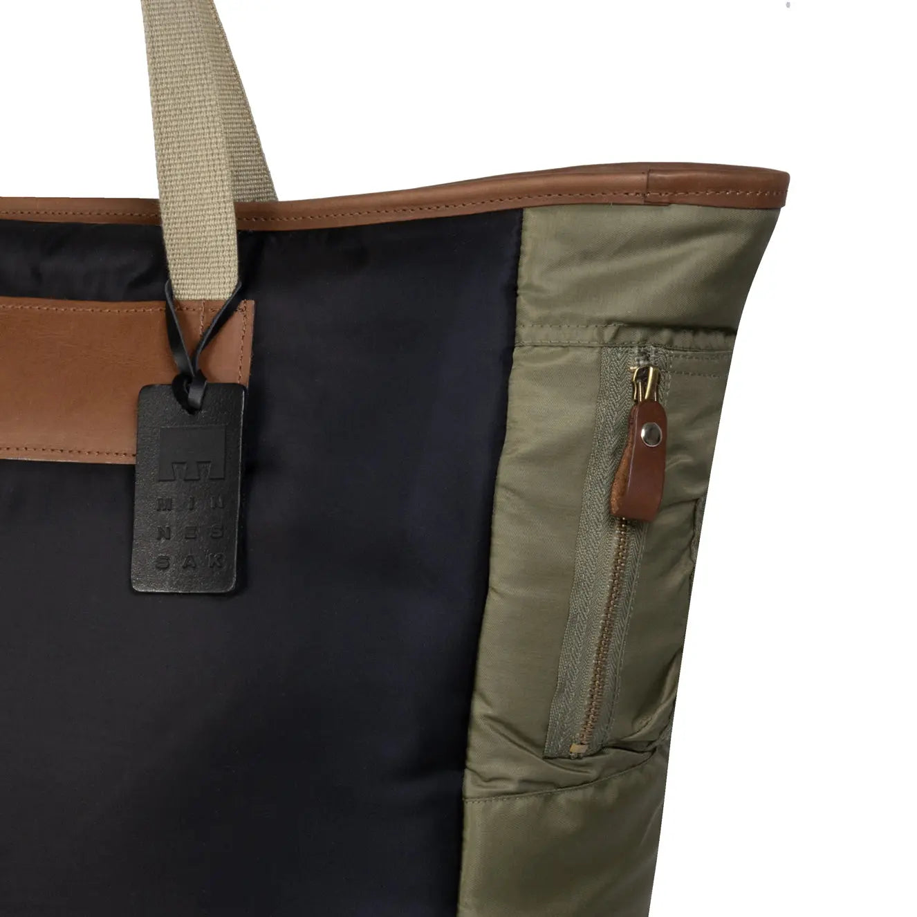 Close-up of a tote bag with a tag, showing black, brown, and olive colors.