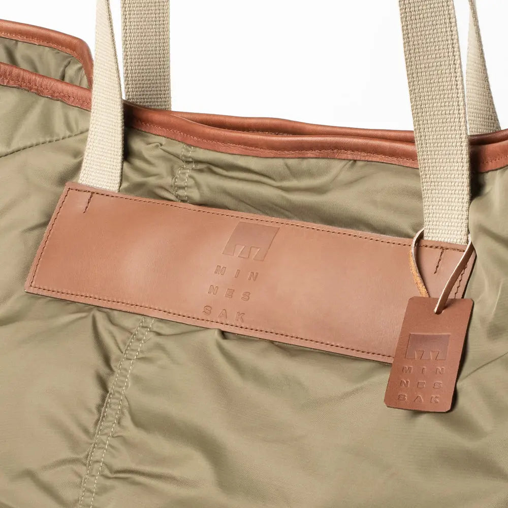 Close-up of an Olive bag with a brown leather patch and tag, featuring the brand 'Minnessak Bag'.