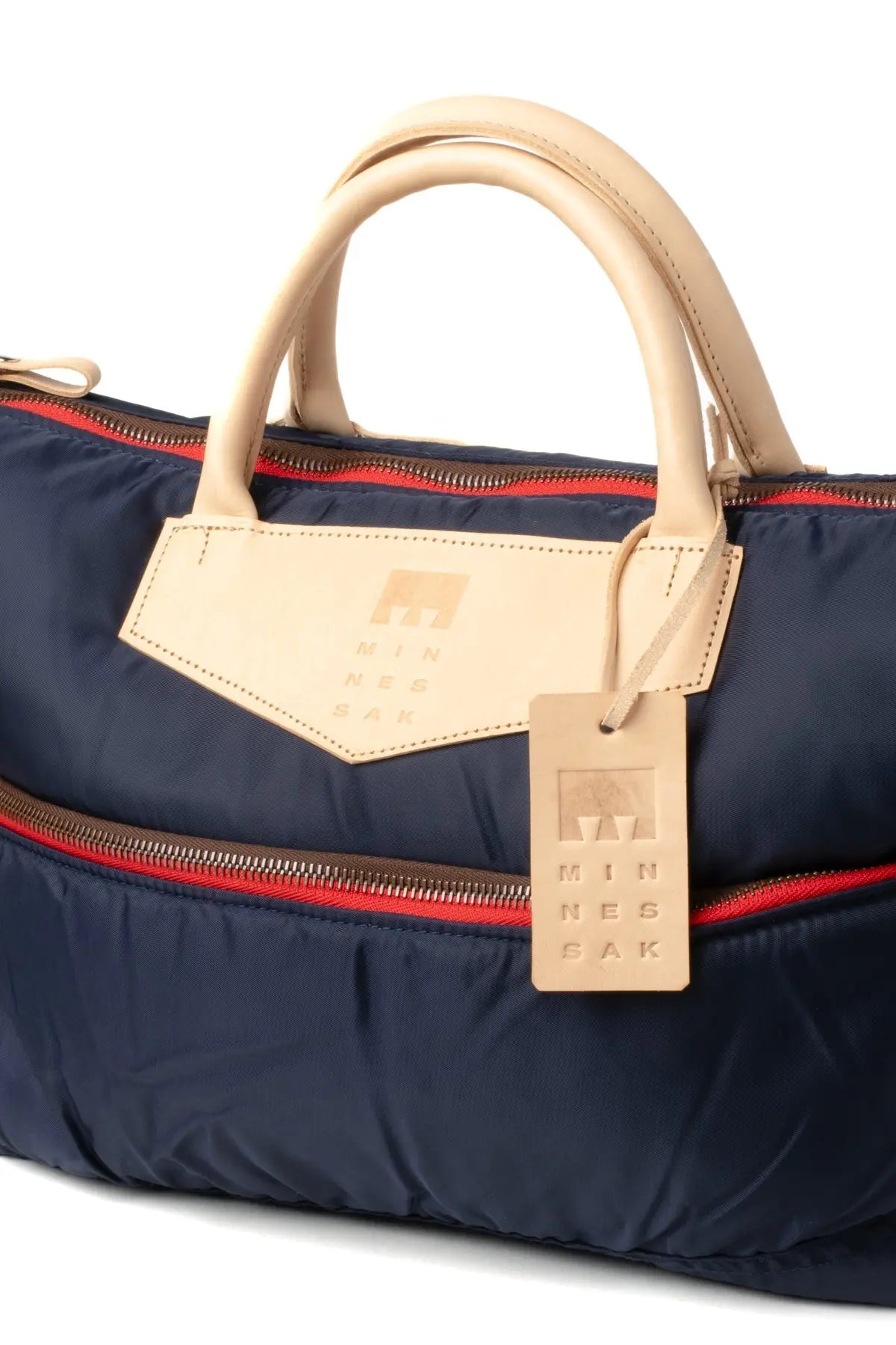 Navy blue handbag with beige handle and tag on a white background