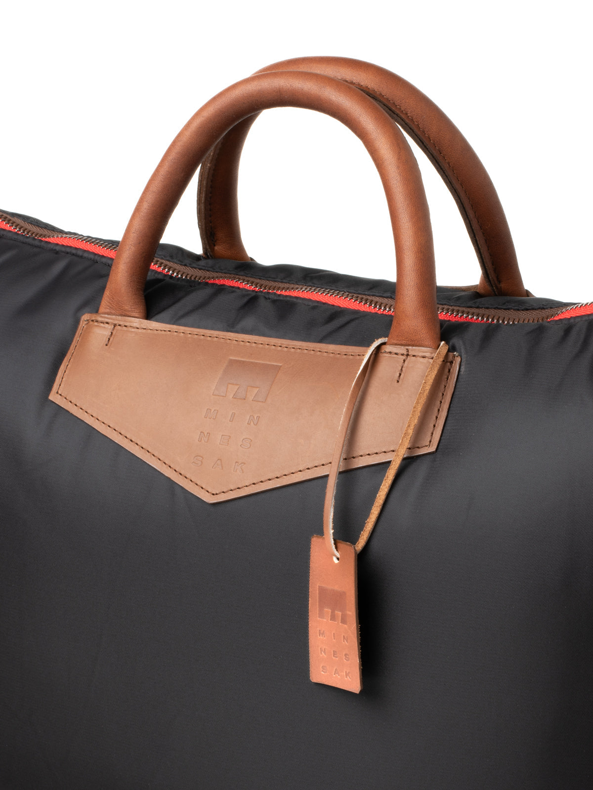 Black bag with brown leather handles and tag on a white background