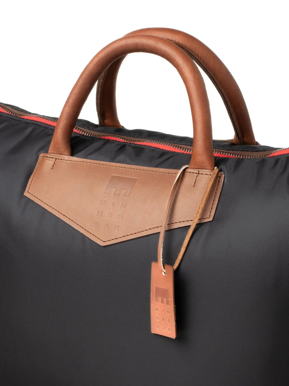 Black bag with brown leather handles and tag on a white background