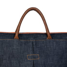 Close-up of a denim bag with brown leather handle on a white background