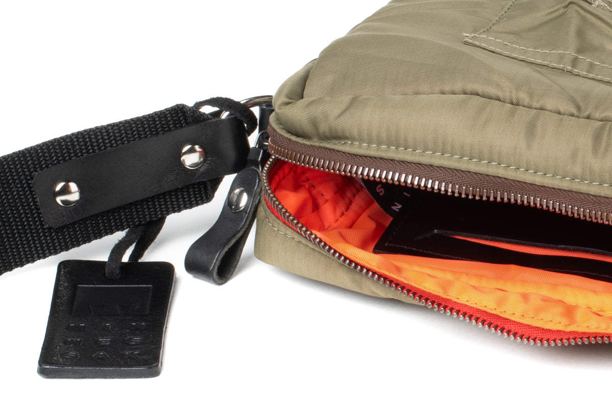 Olive bag with a black strap and orange interior on a white background
