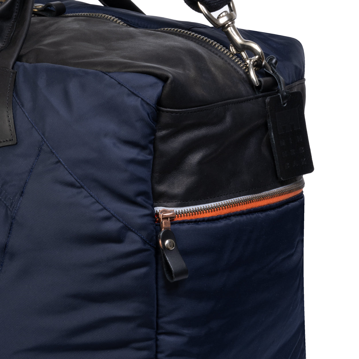 Close-up of a navy blue bag with black leather accents and orange zipper on a white background