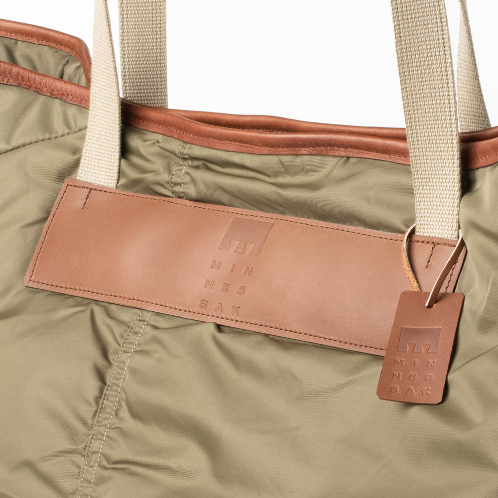 Close-up of an Olive bag with a brown leather patch and tag, featuring the brand 'Minnessak Bag'.
